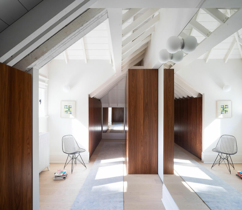 Bright attic space with white walls and exposed beams, wooden partitions, a modern chair, and decorative wall art.