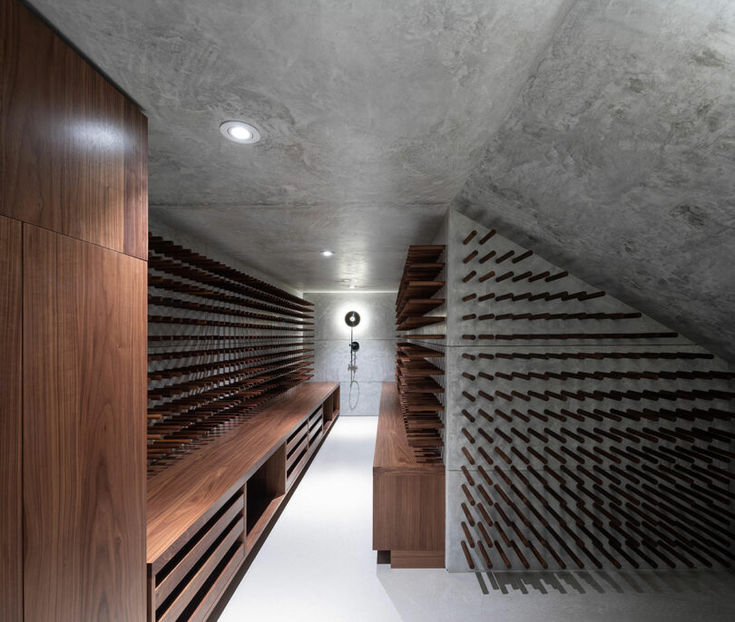 Modern wine cellar featuring wooden racks lining the walls, a central wooden bench, and an exposed concrete ceiling, illuminated by recessed lighting.