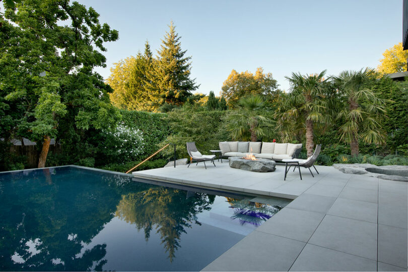 Luxury backyard with a swimming pool, modern patio furniture, and lush greenery under a clear sky.