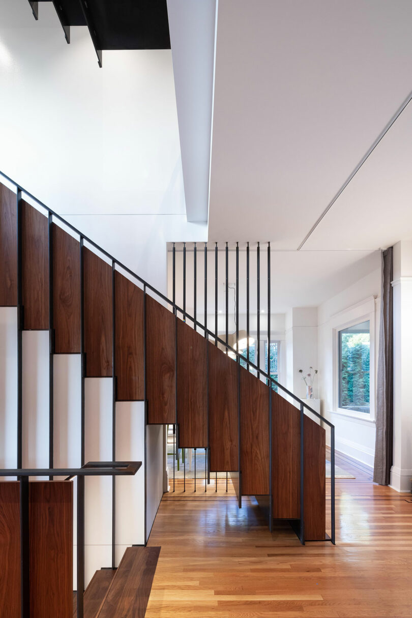Modern staircase featuring warm wood panels and black metal railings in a bright room, complemented by sleek, white decorative elements under the stairs.