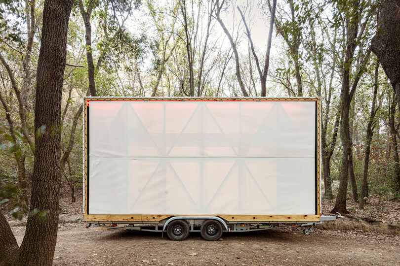 Mobile structure with translucent walls parked in a wooded area.