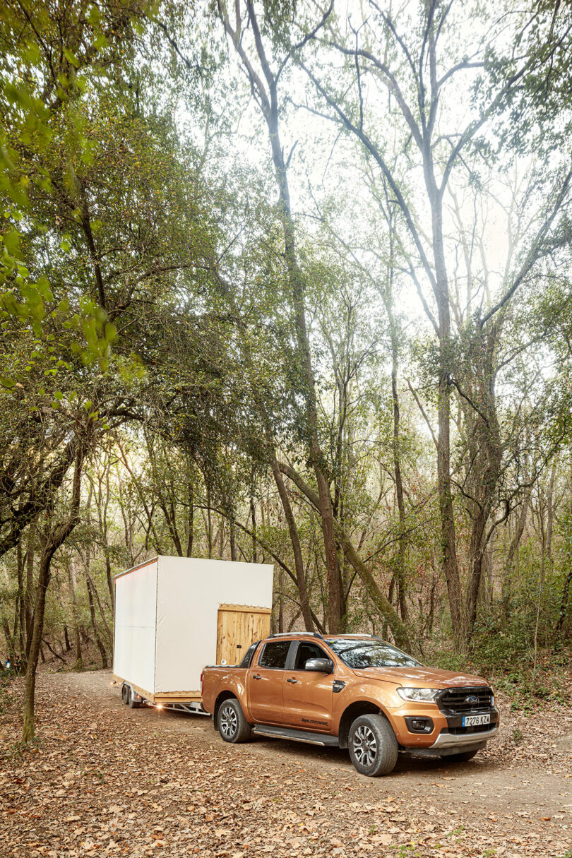 Pickup truck towing a small white trailer on a forest path.
