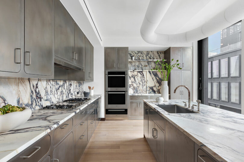 Modern kitchen with stainless steel appliances, marble countertops, and wooden floor, located in a high-rise building with city views.