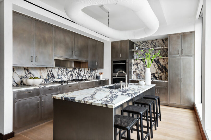 A modern kitchen with stainless steel cabinets, marble countertops, and a central island with bar stools.