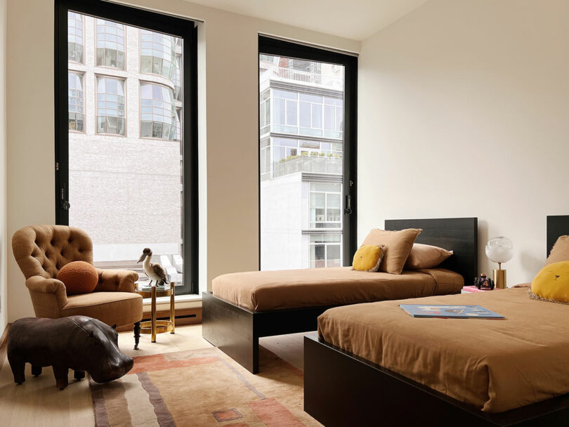 Modern bedroom in featuring two twin beds, large windows with city view, an armchair, and minimal decoration.