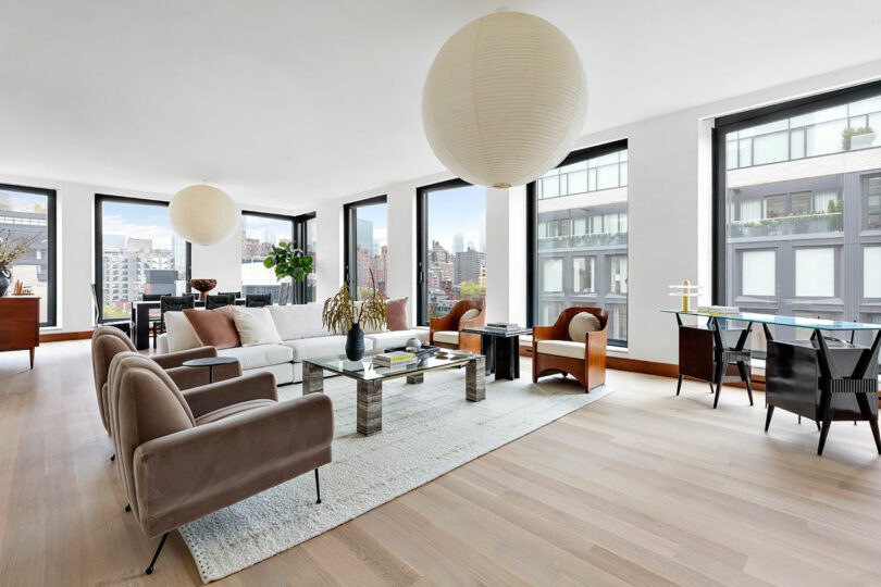 Spacious modern living room in with large windows, leather furniture, and a city view, featuring wooden floors and white walls.
