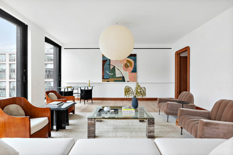 Modern living room with white walls, large windows, a spherical pendant light, contemporary Rockhill artwork, and minimalist furniture including a glass coffee table and plush sofas.