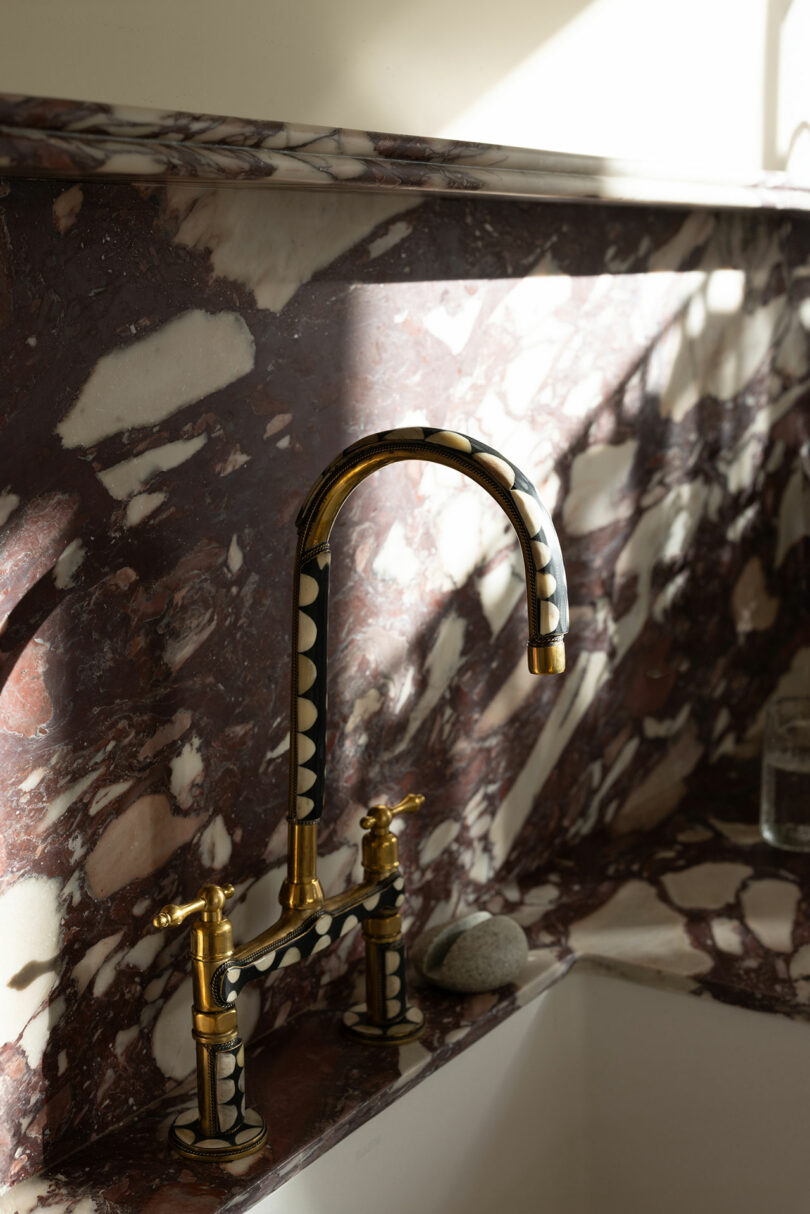 An elegant brass kitchen faucet over a marble sink with sunlight casting shadows on the surface.