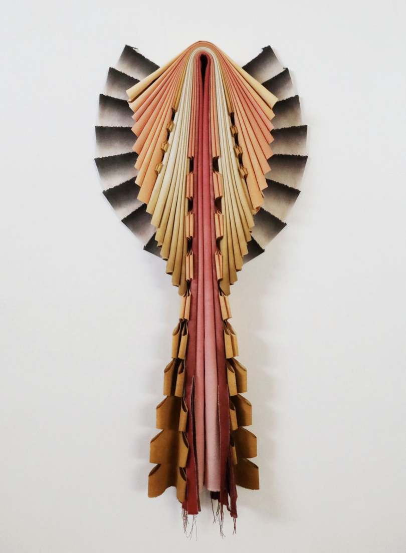 A wall-mounted art piece resembles an open book with pages fanned out above and hanging below.