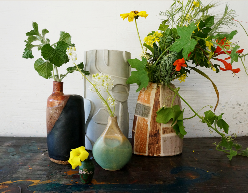 Assorted colorful flowers and greenery arranged in a collection of ceramic vases on a wooden surface.