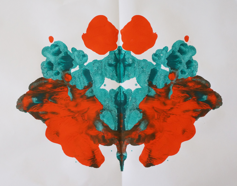 Abstract symmetrical rorschach inkblot in red and teal on white paper.