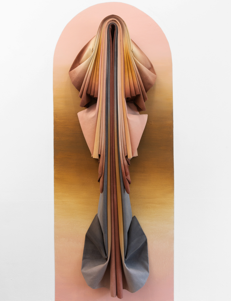 Abstract wall sculpture with layered, draping fabric in warm tones.