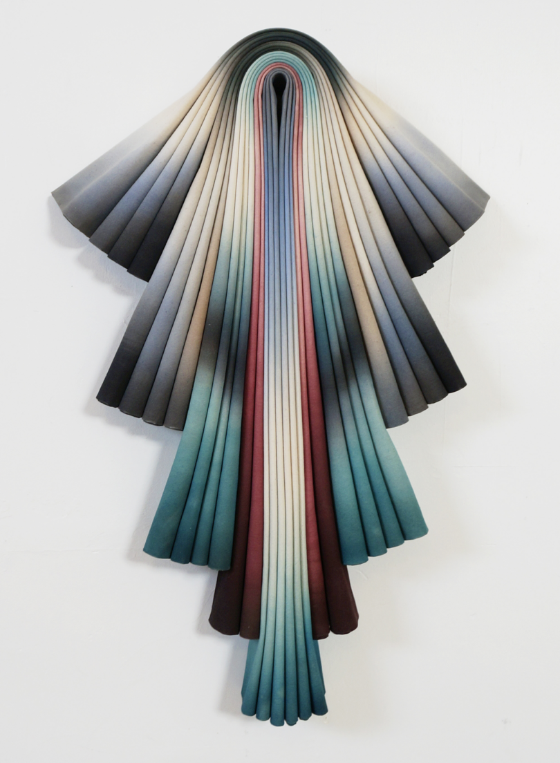 A wall-mounted sculpture resembling an abstract, cascading ribbon in varying shades of white, red, blue, and black.
