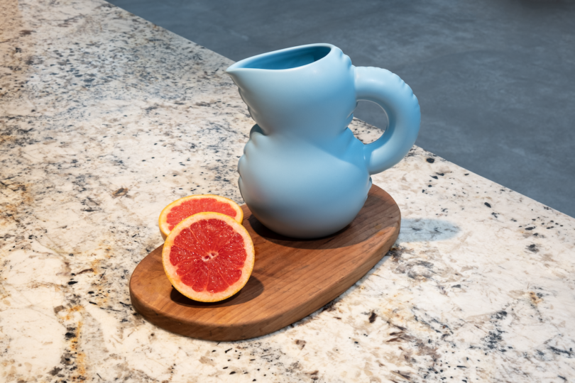 A matte blue ceramic jug on a wooden board with sliced grapefruit, placed on a marble countertop.