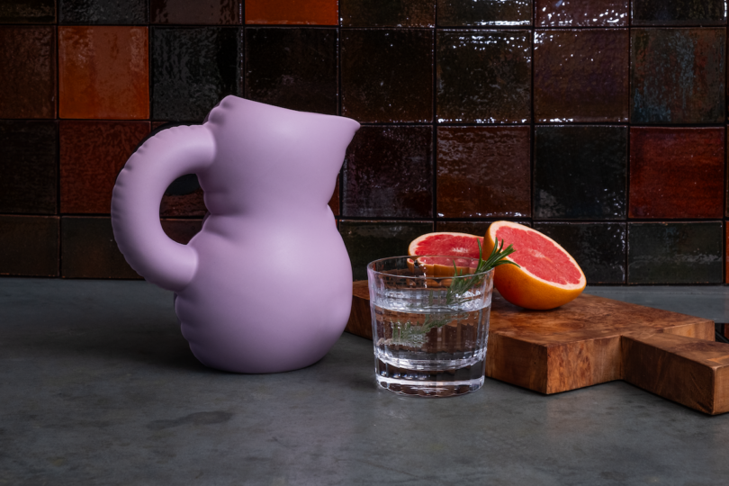 Lavender pitcher, glass of water with mint, and halved grapefruit on a kitchen counter.