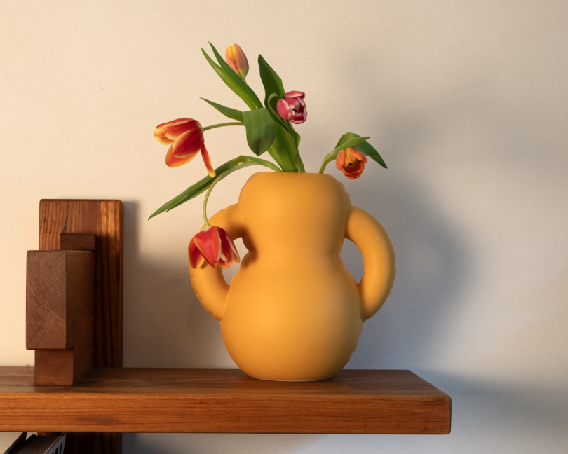 Yellow vase with tulips on a wooden shelf.