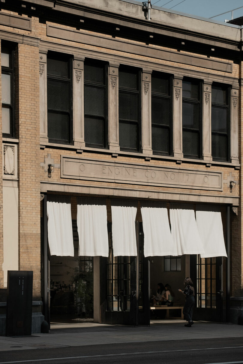 A person walks by a historic building repurposed as a hotel and cafe with white awnings, labeled "engine co no 17.