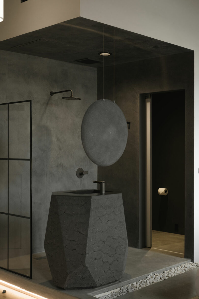 Minimalist bathroom with a monolithic stone sink and mirror, featuring dark textured walls and design elements.