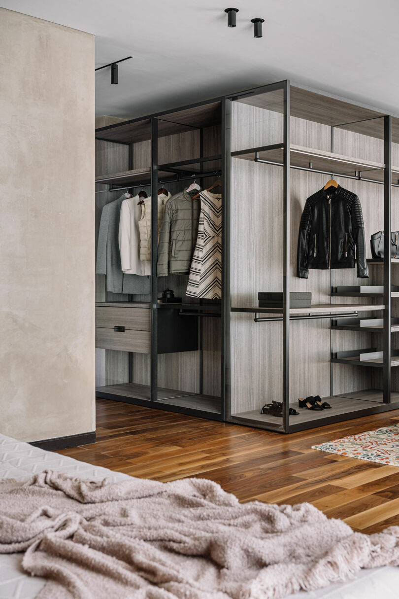Modern walk-in closet featuring an elegant metal and glass wardrobe with neatly organized clothes and shoes, complemented by a cozy, textured blanket in the foreground.