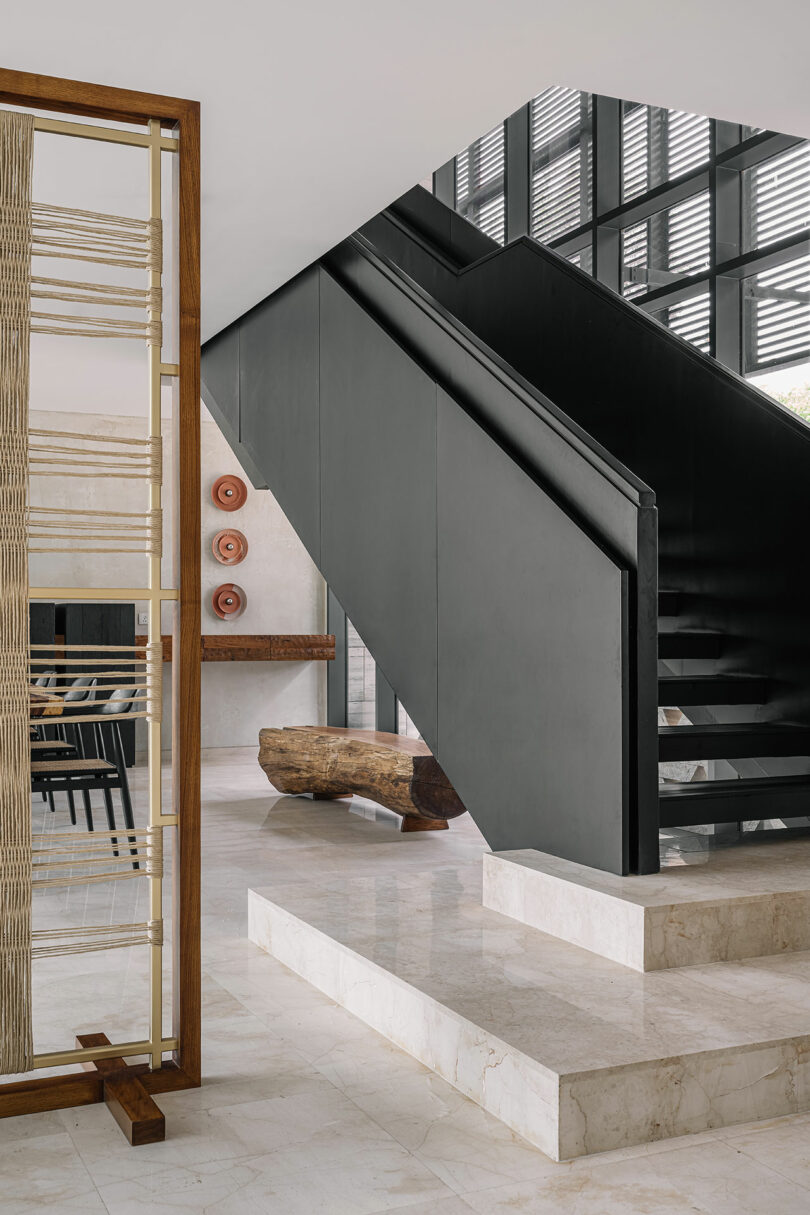 Modern interior featuring a sleek black staircase with white marble steps, a wooden bench, and artistic wall decor.