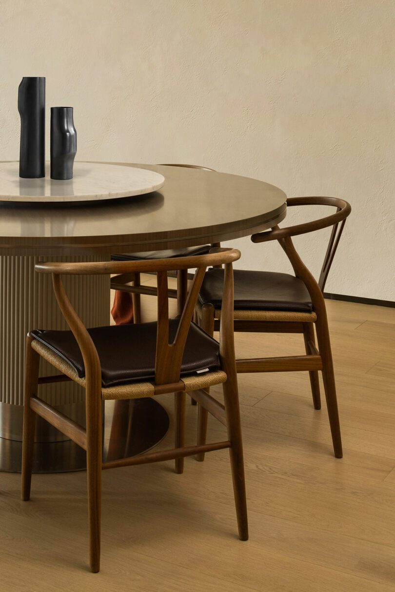 Partial view of modern round dining table with three dark wood Wishbone chairs.