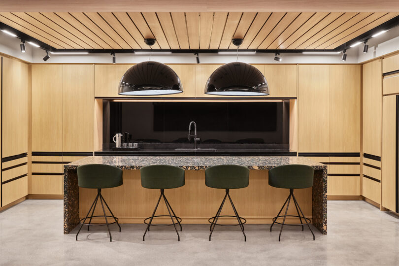 office kitchen with oversized island and two black dome pendants in front of wood cabinetry