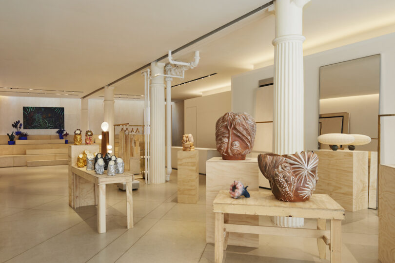 various ceramics and sculptures on wooden tables in a neutral toned clothing store