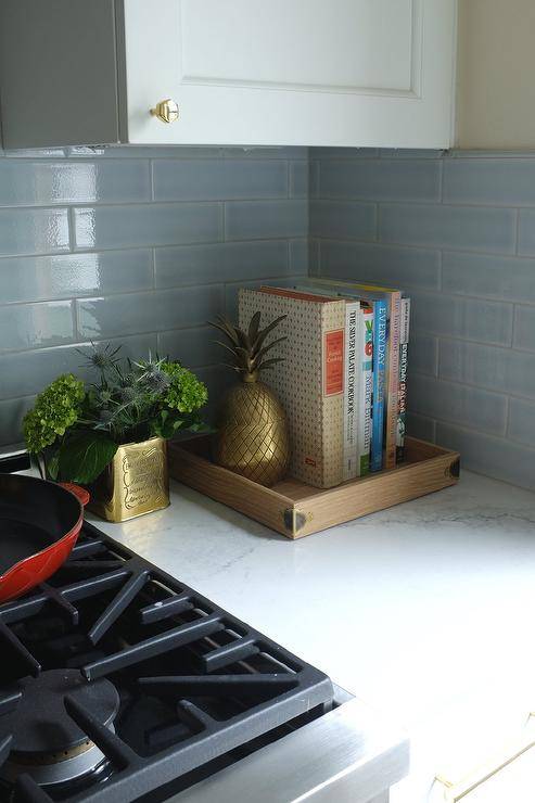 White and gray natural stone countertops in a small kitchen designed with white shaker cabinets and brass knobs. Sky blue subway tiles bring a charming color tone to space upgraded with stainless steel appliances and brass decor.