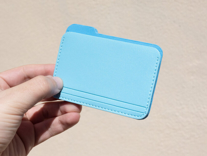 Hand holding a light blue card holder resembling a computer file folder.