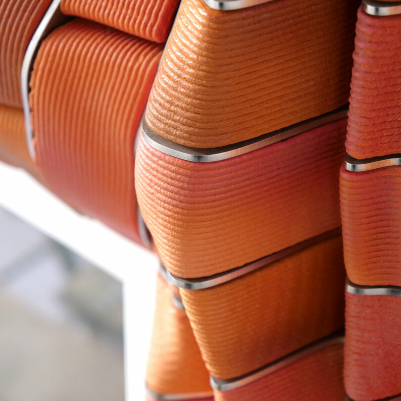 Close-up of tightly stacked orange fire hoses with silver connectors, arranged in a circular pattern on a rack.
