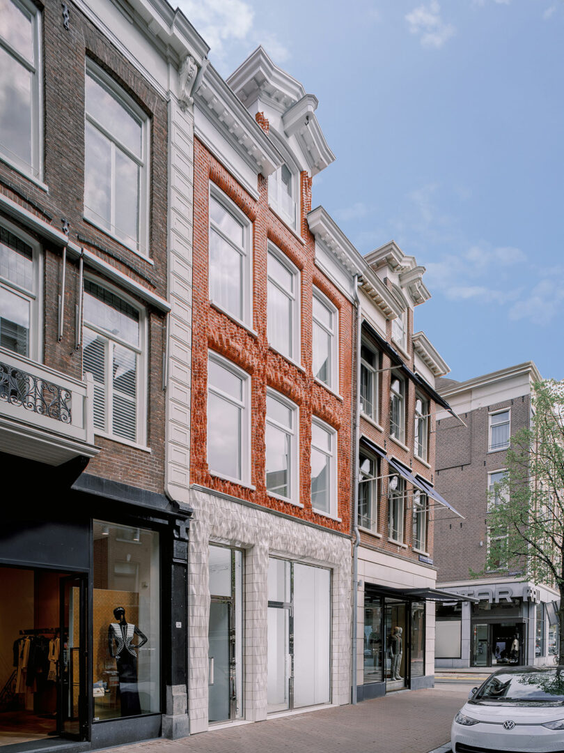 Three-story brick building with retail shops on the ground floor, located on a tree-lined street with parked cars.