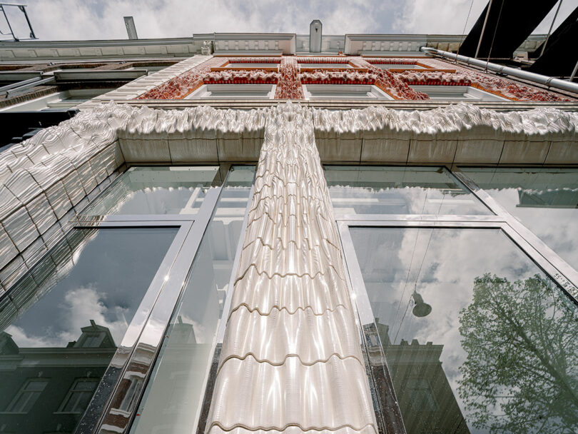 Looking up at a modern building with a shiny, reflective glass facade and detailed, decorative cornices under a clear sky.