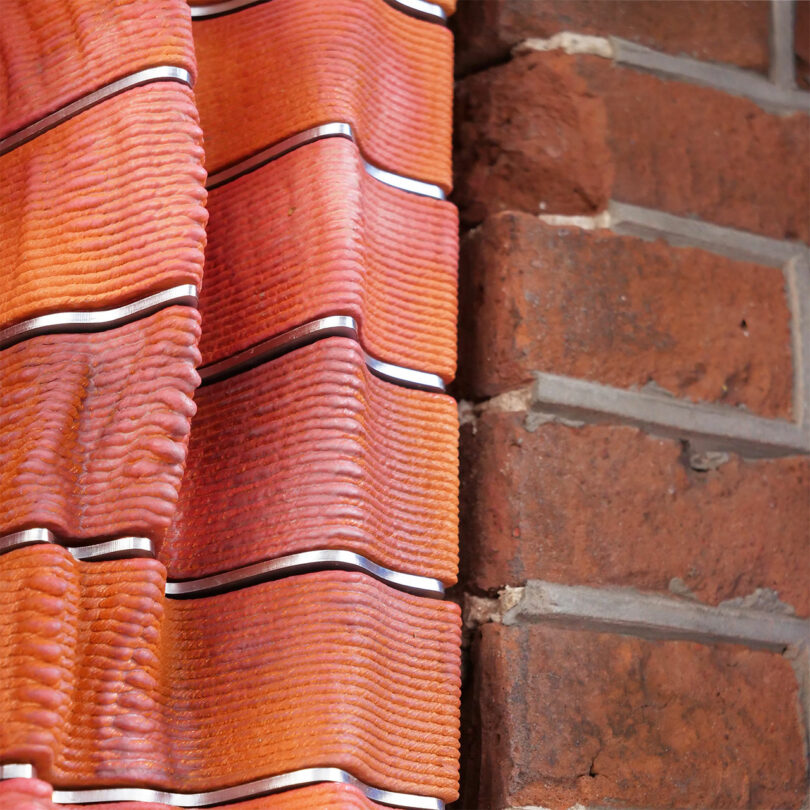 Close-up of red terracotta roof tiles overlapping a brick wall, highlighting contrasting textures and colors.