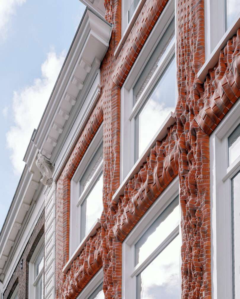 Detailed facade of a building showing windows with unique sculptural brick frames under a cloudy sky.
