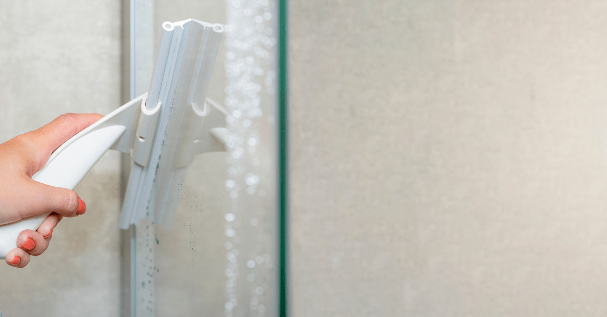 Closeup of someone's hand using a squeegee to clean glass shower.