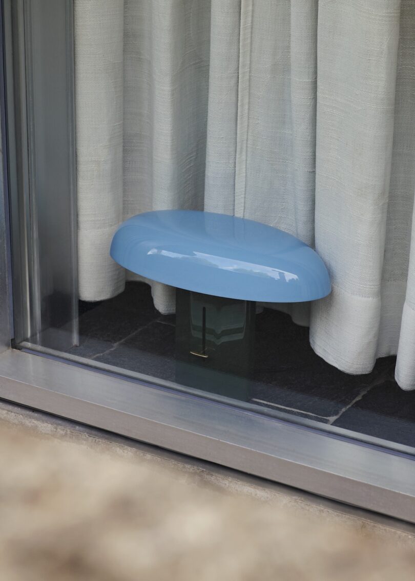 Blue lamp placed in front of a window with curtains.