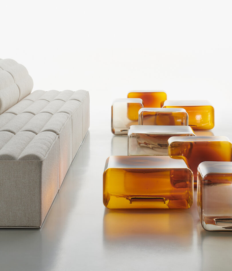 eight translucent and amber glass tables arranged neatly on a white surface next to a white sofa
