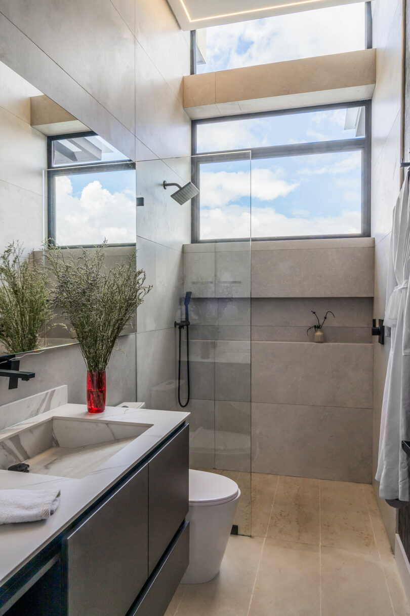 Modern bathroom featuring a glass shower stall, skylight, floating vanity with dual sinks, and neutral tile decor.