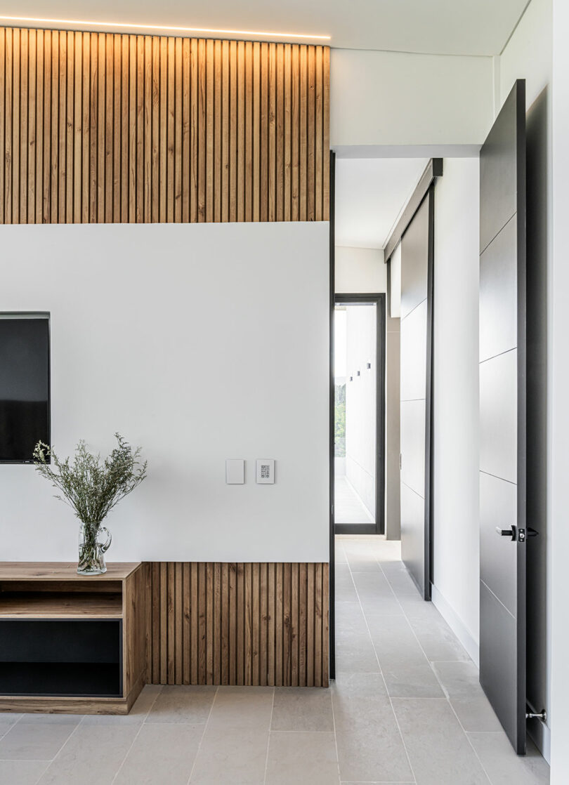 Modern living room corner with wooden paneling, a wall-mounted tv, and a minimalist hallway with grey tile flooring.