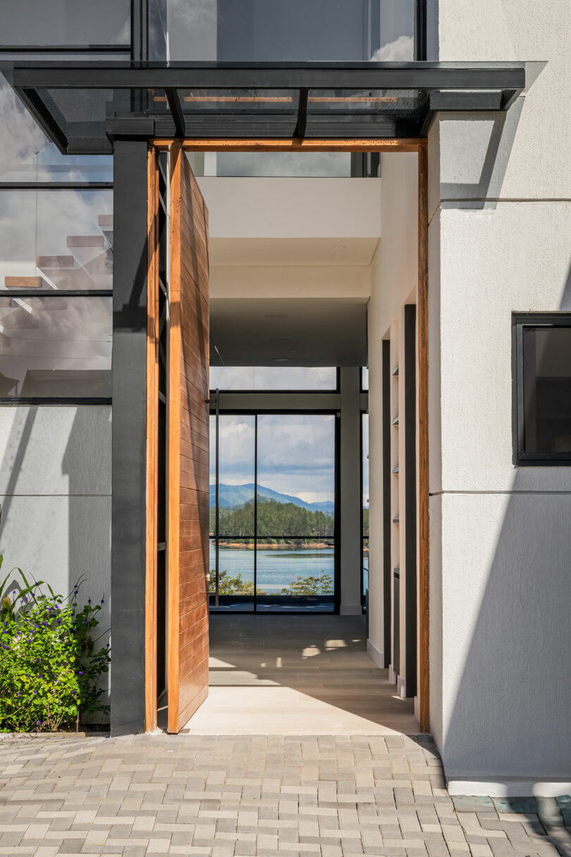 Modern building entrance with glass doors framed by wooden panels and steel beams, overlooking a coastal landscape.