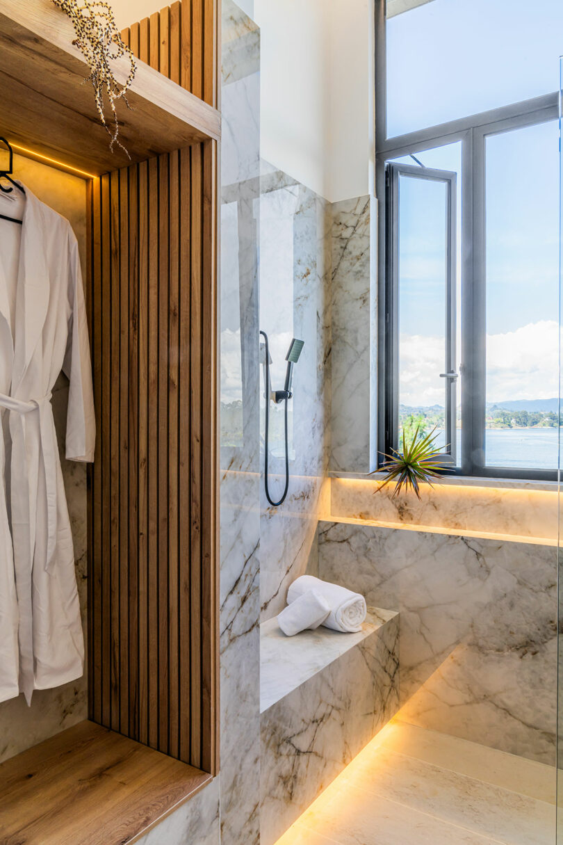 Luxurious bathroom interior with marble walls, a wooden shower area, and a wide window showcasing a lake view.