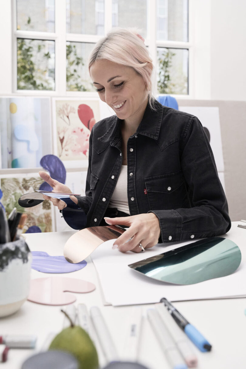 woman holding magnetic shapes at a desk with art supplies in front of a window