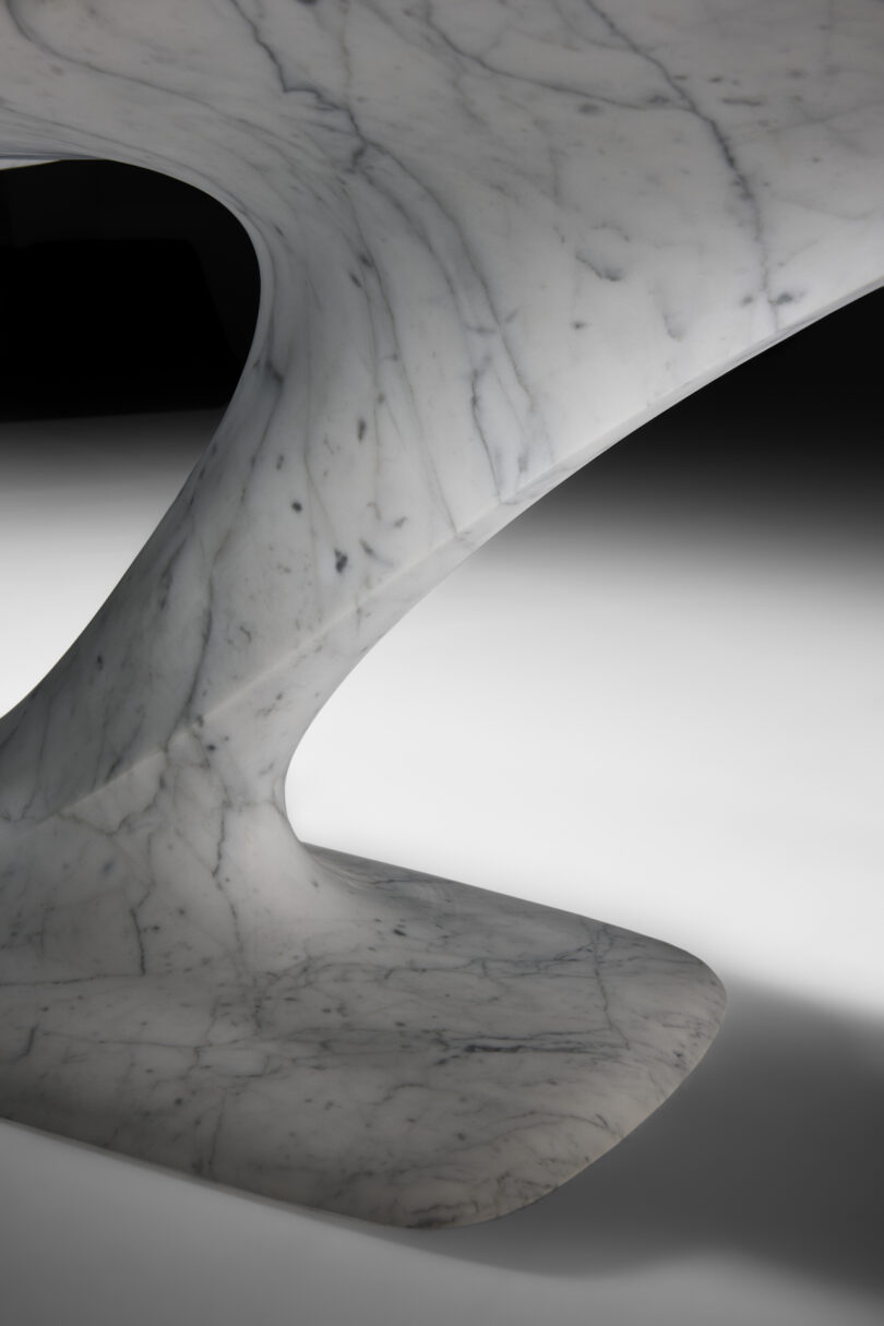 up close details of a modern marble table with a unique v-shaped base and a split, elongated oval top, highlighted against a black background.