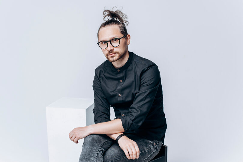 Man in black shirt and glasses sitting.