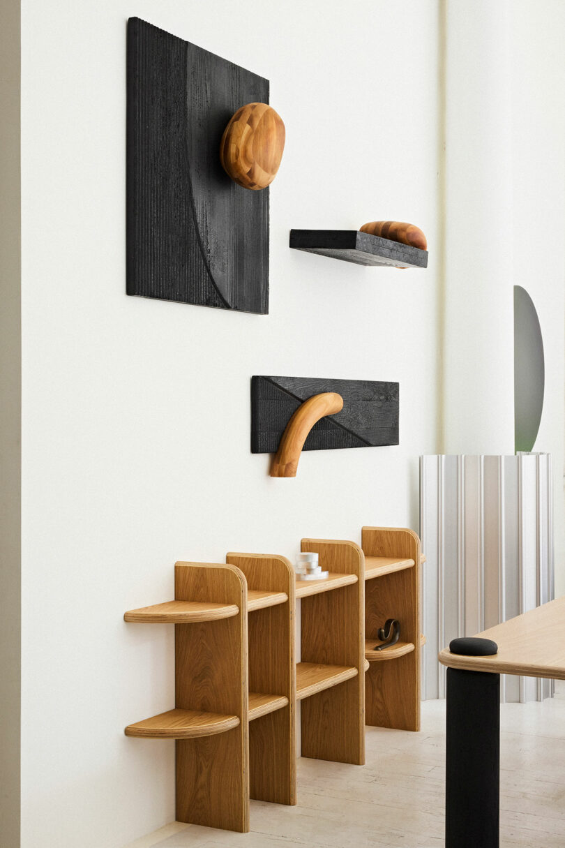 Modern interior with wooden chairs aligned against a white wall, featuring unique black wall panels displaying stylized wooden objects.