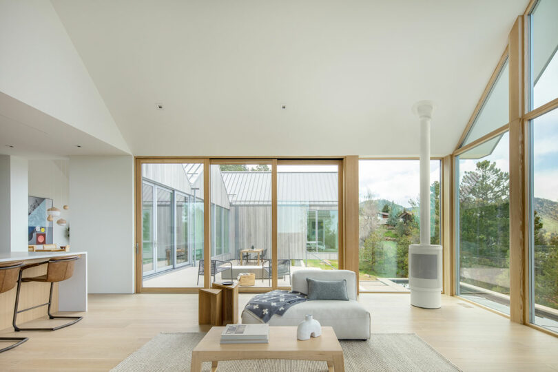 Modern villa H living room with large windows overlooking nature, featuring minimalistic furniture and neutral colors.