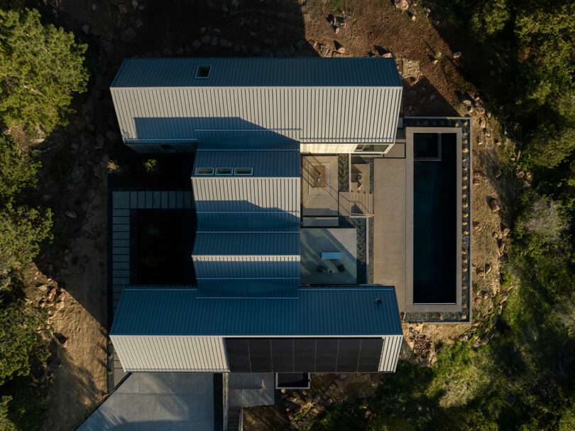 Aerial view of Villa H, a modern geometric house with corrugated metal siding, surrounded by trees, featuring an adjacent rectangular swimming pool.