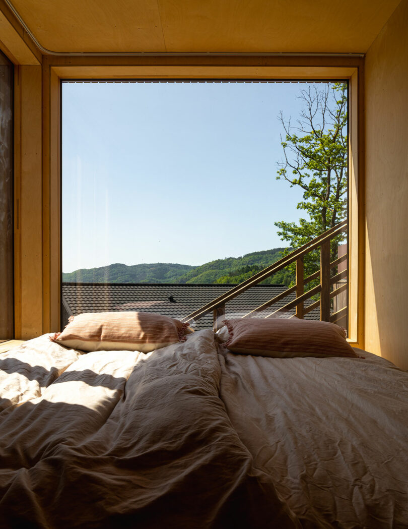 A cozy room with a bed positioned next to a large window offers a picturesque view of green hills and a clear sky.