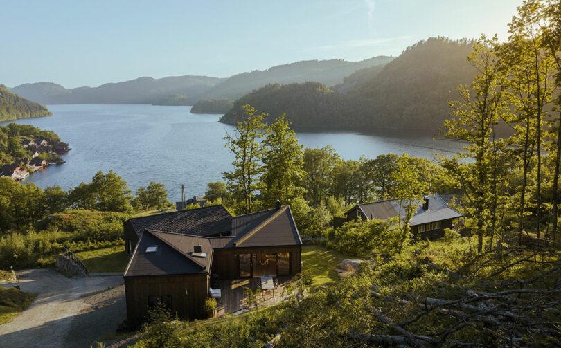 A serene lakeside scene with modern wooden houses surrounded by lush greenery and hills in the background.