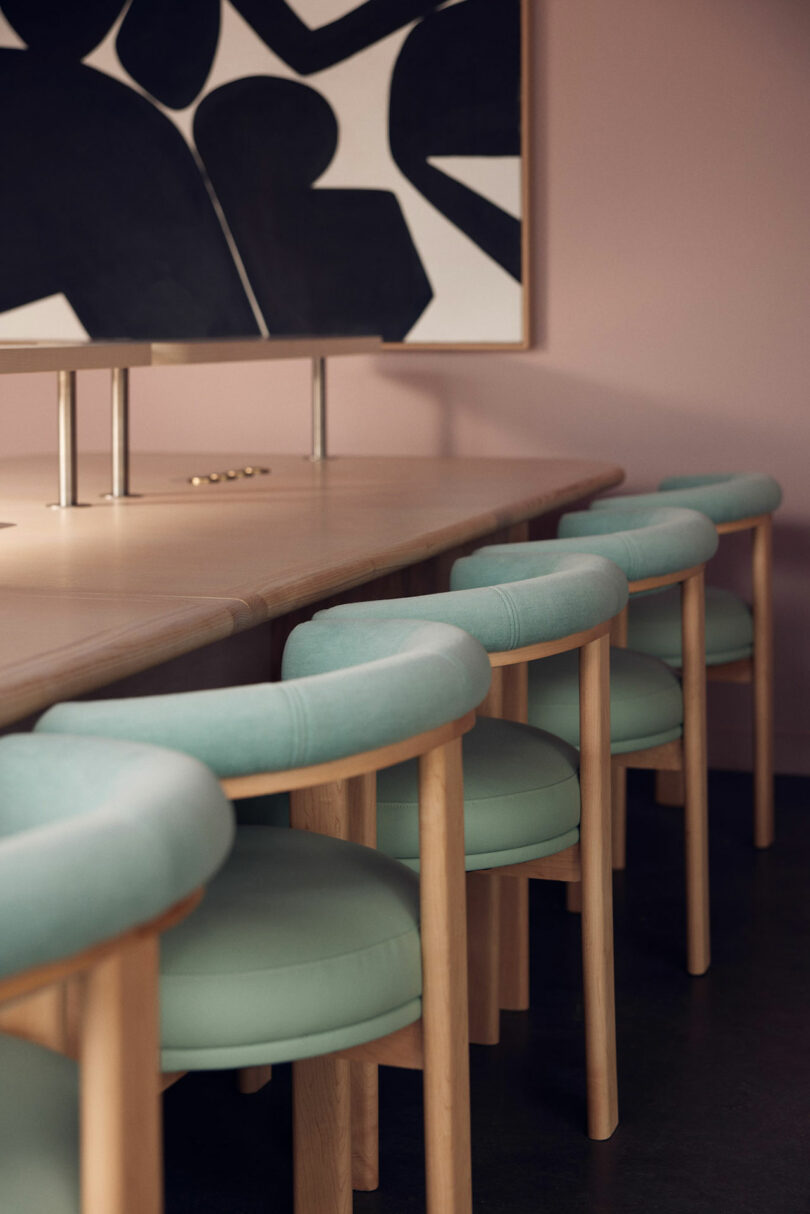 A row of light blue upholstered chairs, designed by Malin, is lined up at a wooden table. A black and white abstract painting hangs on the wall above the table.